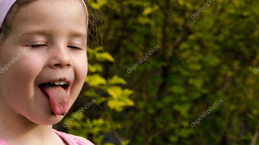 A little girl has been smeared with chocolate and stretches her tongue out