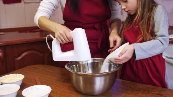 Дочка додає в миску цукор та інгредієнти для змішування матері з мікшером — стокове відео
