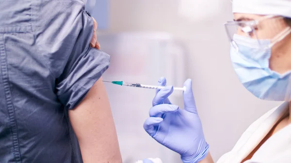 安全手袋と保護マスクの医療看護師は、患者にワクチン注射を行っています。医者は治療として薬物のショットを置くために低血圧針と注射器を使用しています.予防接種 — ストック写真