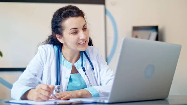 Ärztin im weißen Arztkittel nutzt Laptop, um Patienten aus dem Gesundheitswesen online zu beraten. Ärztliche Online-Sprechstunde. Freundlicher Arzt führt Videogespräche mit Laptop aus der Ferne — Stockfoto