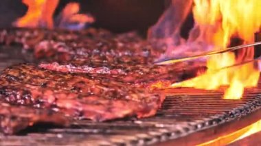 Barbekü ızgara et. Sulu domuz kaburgaları ızgaranın ızgarasında kızartılıyor, Şef kaburgaları Spatula ile çeviriyor..