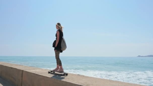 여름날더운 해변의 스케이트보드 위에 있는 아름다운 금발의 소녀 — 비디오