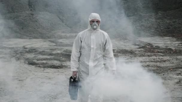 Laboratör i mask och kemisk skyddsdräkt, går på torr mark med verktygslåda genom giftig rök — Stockvideo