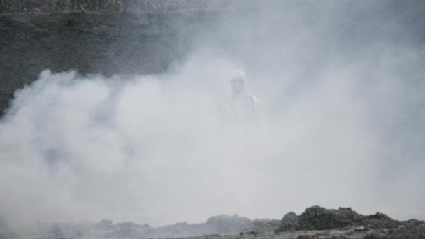 Laboratorní technik v masce a chemickém ochranném obleku, kráčí po suché zemi s krabicí s nářadím přes toxický kouř — Stock video