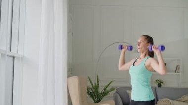 Kız küçük bir dambıl tutuyor ve egzersiz yapıyor. Kadınlar spor ve spor için evlerine giderler..