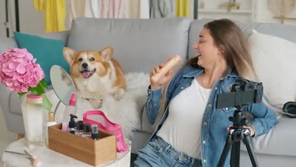 Ein attraktives Teenagermädchen plaudert über Make-up und amüsiert sich dabei mit ihrem süßen Hund. Die Bloggerin führt während des Bloggens Fernunterricht über Kosmetik durch. Der Wind bläst ihr in die Haare. Influencer der neuen Generation — Stockvideo