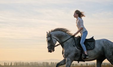 Genç sarışın kız gün batımında bir atın üstünde