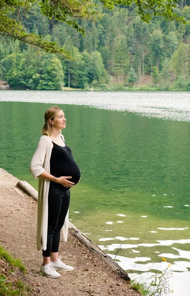 Vacker gravid kvinna nära en fjällsjö i skogen. — Stockfoto