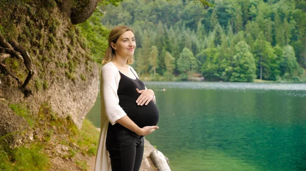 Vacker gravid kvinna nära en fjällsjö i skogen. — Stockfoto
