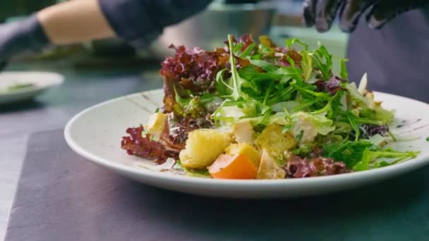 Fechar. Cozinhar. Uma mulher Chef em um uniforme preto em uma cozinha restaurante prepara uma salada de produtos frescos e orgânicos, Caesar Salad. Conceito de comida saudável, close-up. — Vídeo de Stock