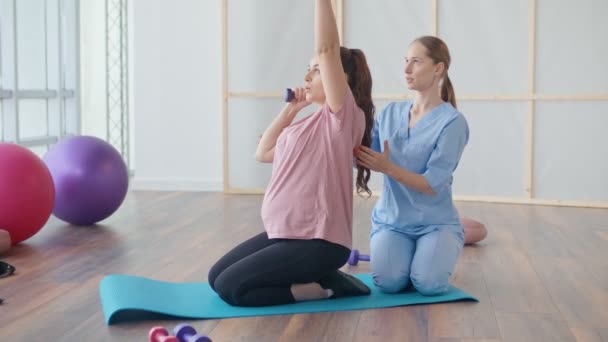 Eine junge schwangere Frau macht in einer Klinik Übungen mit einer Gesundheitshelferin. — Stockvideo
