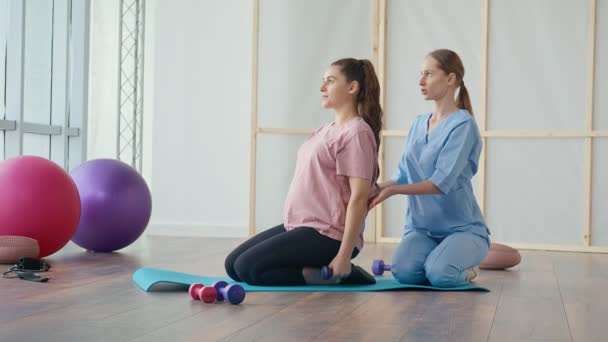 Una mujer embarazada joven está haciendo ejercicios con un trabajador de la salud en una clínica. — Vídeos de Stock