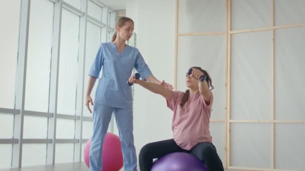 Eine Gesundheitshelferin in einem medizinischen Zentrum hilft einer schwangeren Frau, Übungen zu machen — Stockvideo