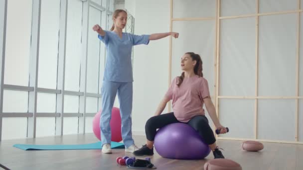 Eine Gesundheitshelferin in einem medizinischen Zentrum hilft einer schwangeren Frau, Übungen zu machen — Stockvideo