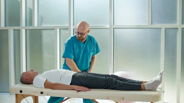 Dospělý muž trénuje sílu svalů s profesionálním lékařem v moderní rehabilitační klinice. Fyzioterapeutický program, rehabilitace po úrazech. Koncepce zdravotní péče — Stock fotografie