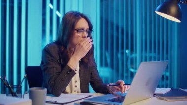 Yorgun bir iş kadını ofiste geç saatlere kadar oturur, bilgisayarında çalışmak için esneme ve mücadele eder. İşyeri Yorgunluğu, Uzun Saatler ve Üretken Kalmaya Çalışırken Yorgunluk kavramı