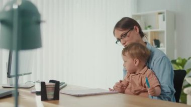 Yaşam Tarzından Herhangi Bir Yerde Çalış. Genç Anne, Çocuğa kucak açarken, Aile Dostunu Gösterirken Ofis Masasında Çalışmaya Çalışıyor 