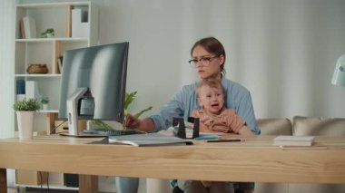 Doğum izni ve ebeveyn desteği. Yorgun Anne, Huzursuz Yürüyen Çocuk 'u Tutarken Bilgisayarda Ofis Çalışmalarını Yönetmeye Çalışıyor 