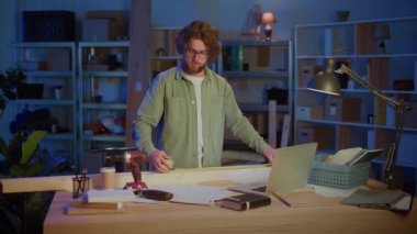 Garaj atölyesinde dizüstü bilgisayarla ahşap kalasları ölçen adam. Marangozluk, Ev Yenileme, DIY Projeleri, Ahşap Planlama ve Modern Yaratıcı Çalışma Alanı Konsepti.