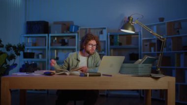 Sınav Hazırlığı. Genç bir erkek öğrenci, akademik baskı altında sıkı çalışmayı, odaklanmayı ve eğitime bağlılığı sembolize eden kitaplar ve bir dizüstü bilgisayarla gece geç saatlere kadar çalışır..