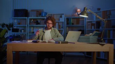 Sınav Hazırlığı. Genç bir erkek öğrenci, akademik baskı altında sıkı çalışmayı, odaklanmayı ve eğitime bağlılığı sembolize eden kitaplar ve bir dizüstü bilgisayarla gece geç saatlere kadar çalışır..