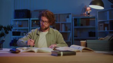 Genç adam gece çalışması sırasında not almaya odaklanmış. Eðitim, araþtýrma, öðrenme, bilgi geliþtirme, sınav hazýrlanmasý ve çok çalýþma ile akademik adanmışlýk kavramı.