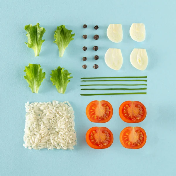 Creative neatly arranged fresh food layout with lettuce, garlic, pepper, chives, cherry tomatoes, rice on blue background. Minimal healthy food concept. Flat lay.