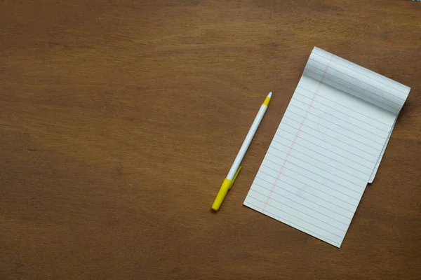 Notepad without writing next to pen on wooden table