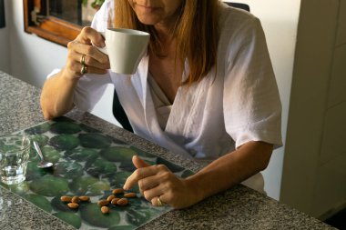 Oturmuş kahve içen ve badem yiyen bir kadın.