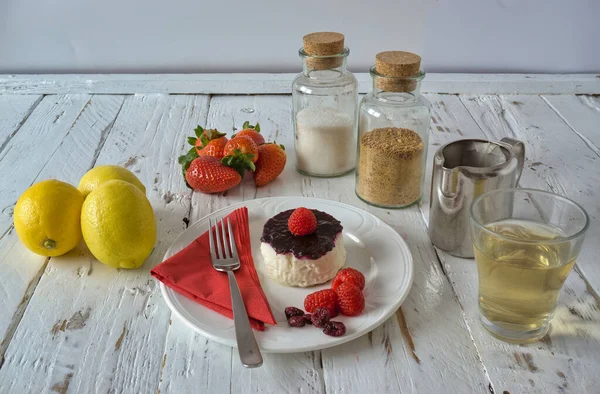 Kırsal ahşap masa üzerinde taze kırmızı çilekli cheesecake, taze limon, çilek ve çay.