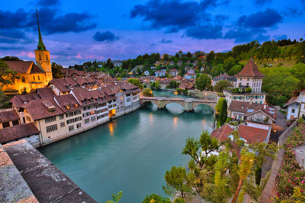 Skyline of Bern, capital of Switzerland at blue hour reflecting in Aare river. Panoramic view of old city, Nydegg Church and Untertorbrucke bridge. Landmark of historical town UNESCO World Heritage.