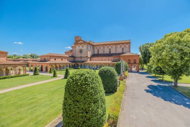 Ferrara Charterhouse of Ferrara Kilisesi, İtalya 'nın Ferrara şehrinde yemyeşil çimenler ve ağaçlar arasında berrak mavi bir gökyüzü altında görkemli bir şekilde yükselir.