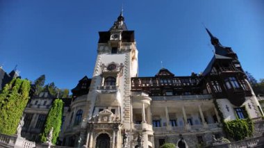 Pele Kalesi, göz kamaştırıcı Neo-Rönesans kraliyet sarayı, Romanya 'nın Transilvanya kentinde özenle hazırlanmış mimarisi, taş sütunları ve canlı yeşil tırmanma sarmaşıklarıyla açık mavi gökyüzüne karşı duruyor.