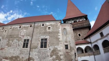 Corvin Castle avlusunda, Hunedoara, Romanya ve Transilvanya 'da açık mavi gökyüzünün altında belirgin bir konik çatı kulesine sahip iç gotik bir cepheye giden ortaçağ kemerli bir kütük bulunuyor.