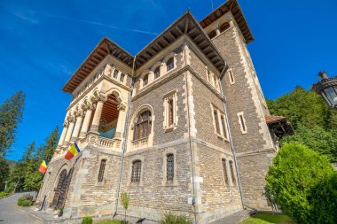 Busteni 'nin tarihi bir simgesi olan Cantacuzino Şatosu, Romanya ve Transilvanya' nın açık mavi gökyüzü altında mimarisini ve bir Romanya bayrağını gösteriyor