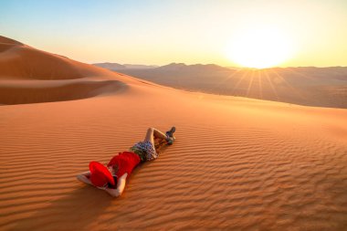 Ummani kumlarında gün batımında bir kız, güneşin batışına tanıklık ediyor Umman 'ın boş çeyrek çölünün kumullarının ötesinde ya da Rub al-Khali.