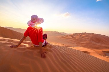 Umman Çölü 'nde güneşin doğuşuna tanıklık eden kırmızı üniformalı bir kız Umman Çölü' nde veya Rub al-Khali 'de..