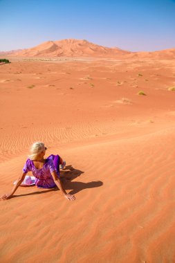Boş Mahalle 'nin sonsuzluğunda kırmızı elbiseli ve şapkalı bir kadın şafak vakti altın kumla çarpıcı bir tezat içinde tek başına. Umman Rub al-Khali çölünde macera ve yalnızlık arıyor..
