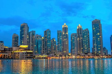 Dubai şehir merkezi, Birleşik Arap Emirlikleri 'nin silueti, Burj Gölü' nün sakin sularına yansıyarak, alacakaranlık gökyüzünün altında bulunan yüksek yerleşim yerlerinin modern bir şehir manzarasını sunar.