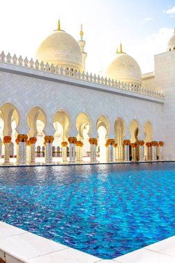 Abu Dabi 'nin Şeyh Zayed Büyük Camii, büyük kemerleri ve kubbeleri, Birleşik Arap Emirlikleri' ndeki parlak bir gökyüzünün altında, etrafındaki havuzun sakin mavi sularına yansıyor.