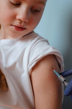 Ampoules with Covid-19 vaccine. Doctor vaccinating cute little boy on blue background, closeup.