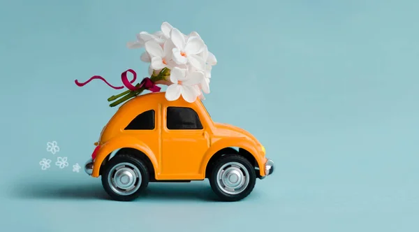 Poltava, Ukraine-May 20, 2021 Orange retro car delivers flowers. A toy car carries a bouquet of white lilac flowers for a gift on a blue background. — Stock Photo, Image