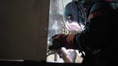 shot from below, a worker in a welder's mask with a drawing at the factory welds a pipe, sparks fly, slow-mo