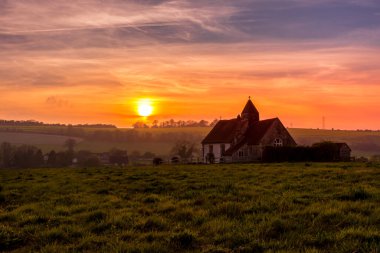 Idsworth 'taki South Downs Ulusal Parkı' nda gün batımında izole St. Hubert kilisesi ve dramatik turuncu ve mavi bir gökyüzü.
