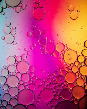 Su yüzeyindeki küçük yağ damlası kabarcıkları pembe ve sarı arkaplanda soyut.