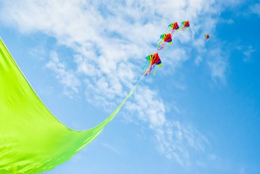 Gökkuşağı renkli uçurtmalar canlı yeşil bir kurdelenin ucunda yüksekten uçuyor Yazın mavi gökyüzüne ve açık bulutlara karşı