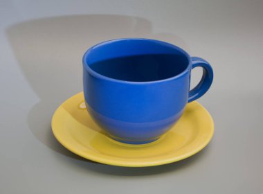 Sarı tabakta mavi çay fincanı, gri arka planda gölgesi var.