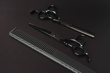Gri Tarak ve Siyah Makas Karanlık Arkaplanda. Profesyonel Saç Aletleri. Minimalist stil