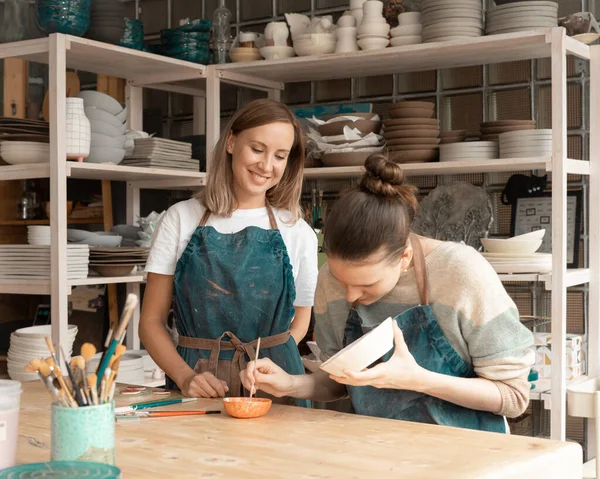 Woman making ceramic pottery. Attractive skilled young lady in apron standing at table and teaching