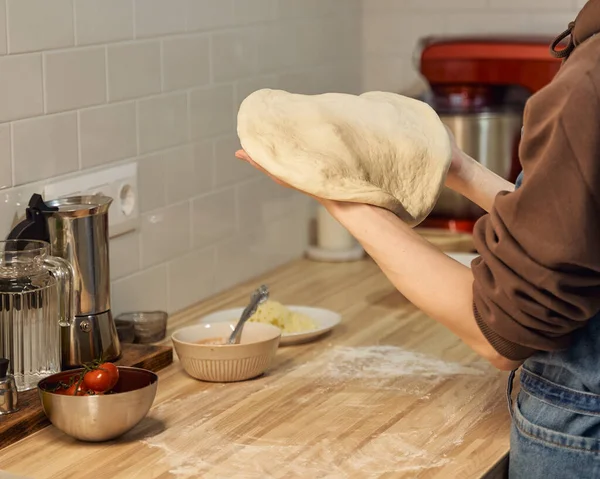 Faceless woman kneading dough on kitchen table at home, apartment. Homemade food